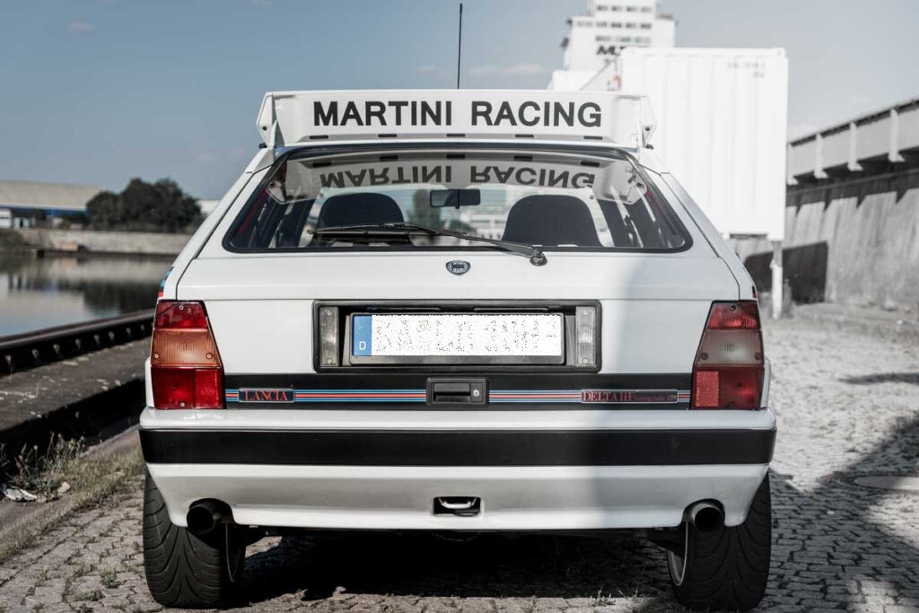 Nahaufnahme des Hecks eines Lancia Delta HF Integrale EVO 16V, aufgenommen von hinten. Die blau-roten Streifen sind sichtbar und der Heckspoiler ist beschriftet mit 'Martini Racing'