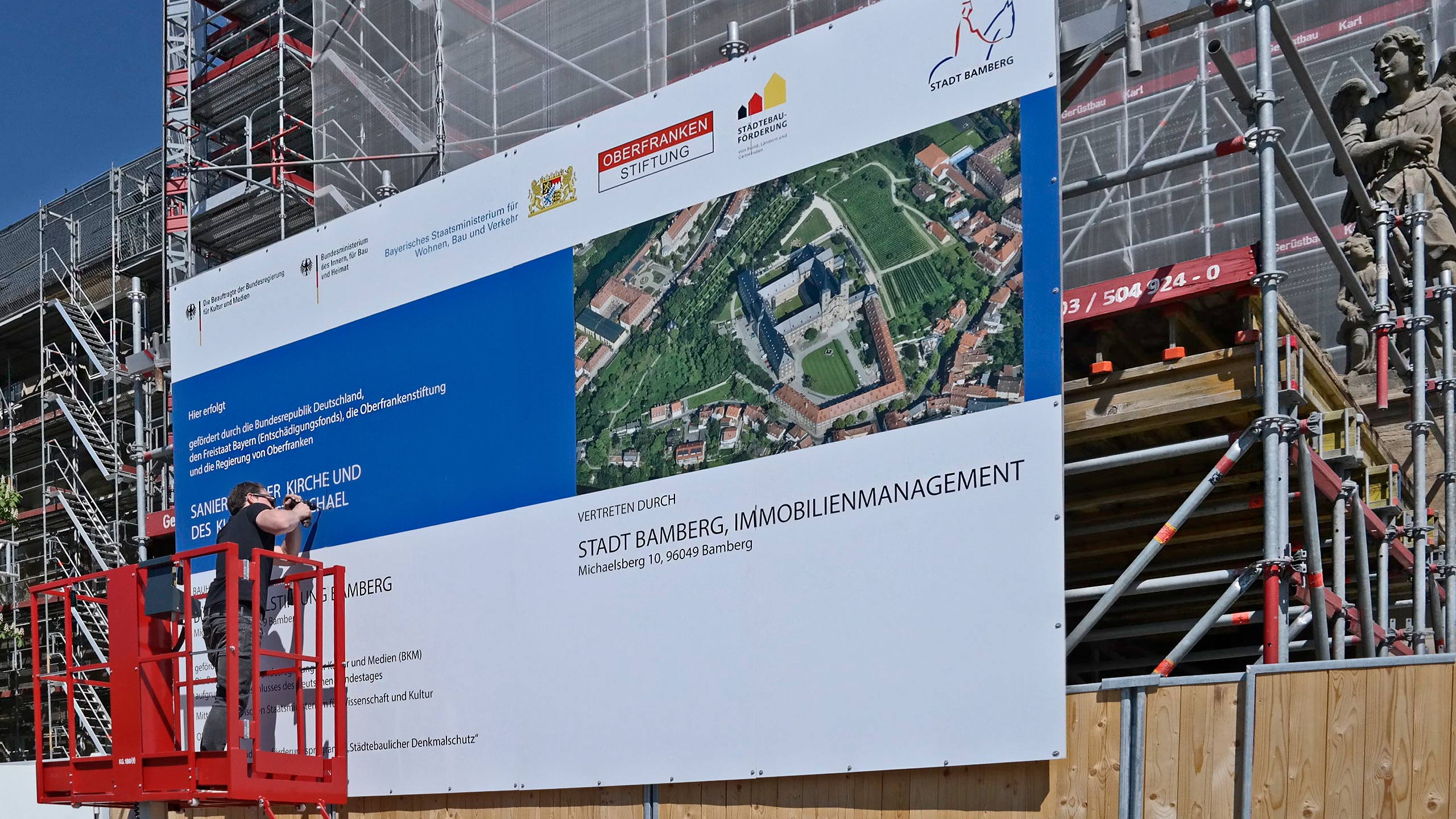 Große Bautafel wird mit einem Kran an einem Gerüst befestigt – Bauprojektvisualisierung