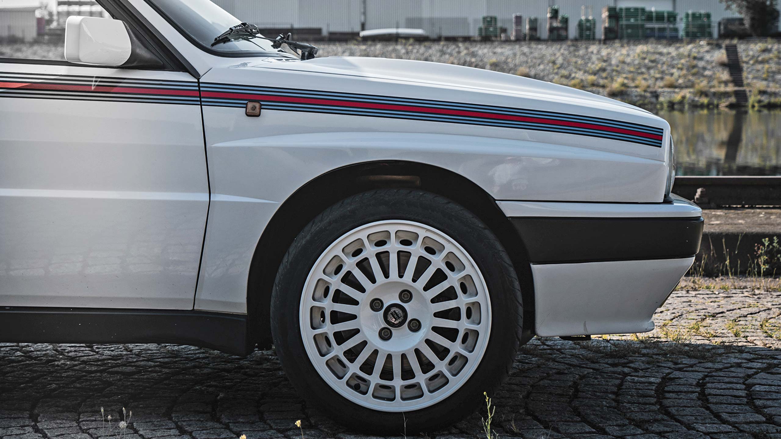 Detailansicht eines folierten Lancia Oldtimers mit originalgetreuen Rallyestreifen in Blautönen und rot.