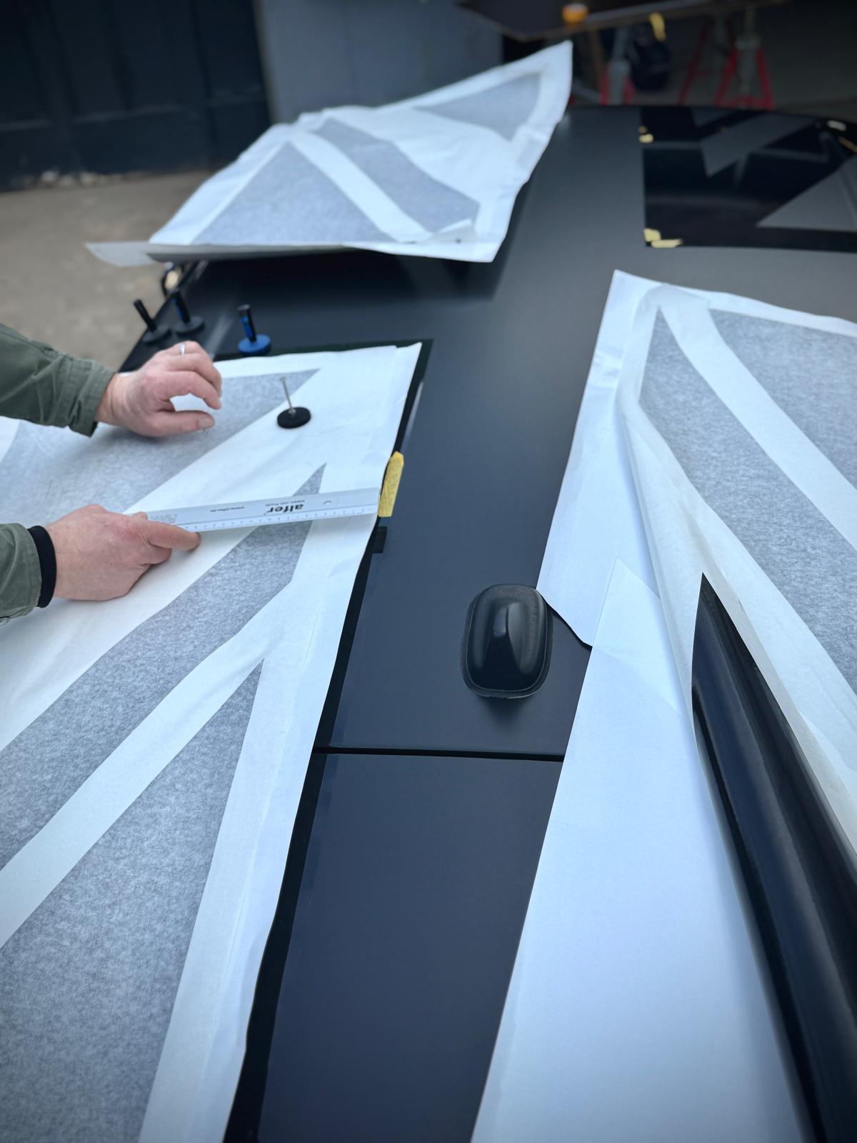 Schwarzer BMW Mini von oben während das Dach mit mattschwarzer Folie foliert und gerade ausgemessen wird.